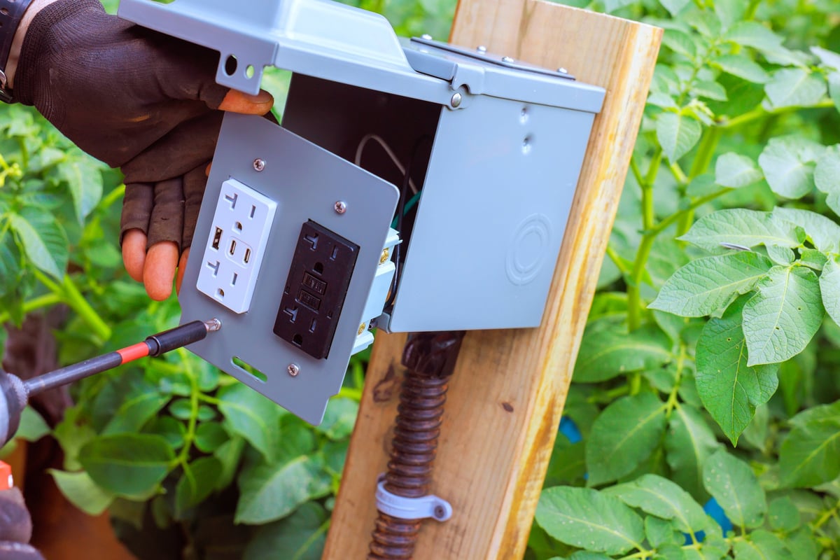 Electrician connects electrical components to box mounted outlet, USB ports on wooden post
